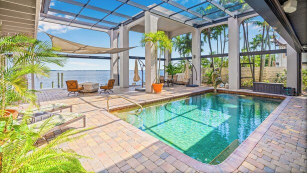 A pool area with clear blue water, surrounded by lounge chairs and potted plants. - VRCC Villa Dolphin House (Cape Coral)