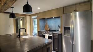A modern kitchen with a large island, stainless steel appliances, and a rustic ceiling.
