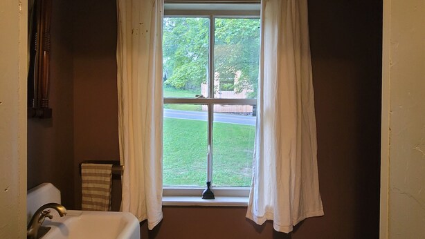 A bathroom with a bathtub, a window with curtains, a ceiling fan, and a toilet paper holder.