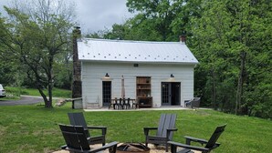 A white house with a stone chimney, a fire pit, and outdoor seating.