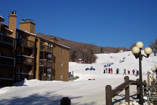 A ski resort with a building featuring balconies and a ski slope in the background.