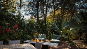 Un patio al aire libre con una chimenea, mobiliario y abundante vegetación.