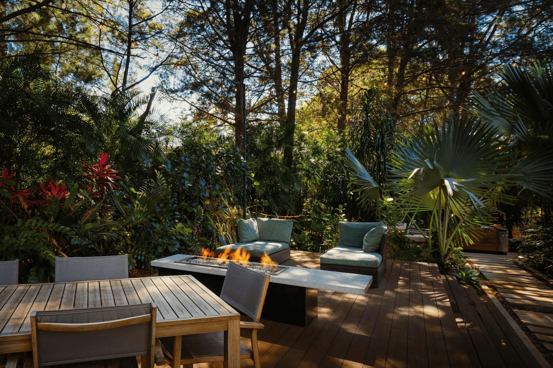 An outdoor patio with a fire pit, seating area, and surrounding lush vegetation.