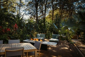 Un patio exterior con un brasero, zona de estar y abundante vegetación circundante.
