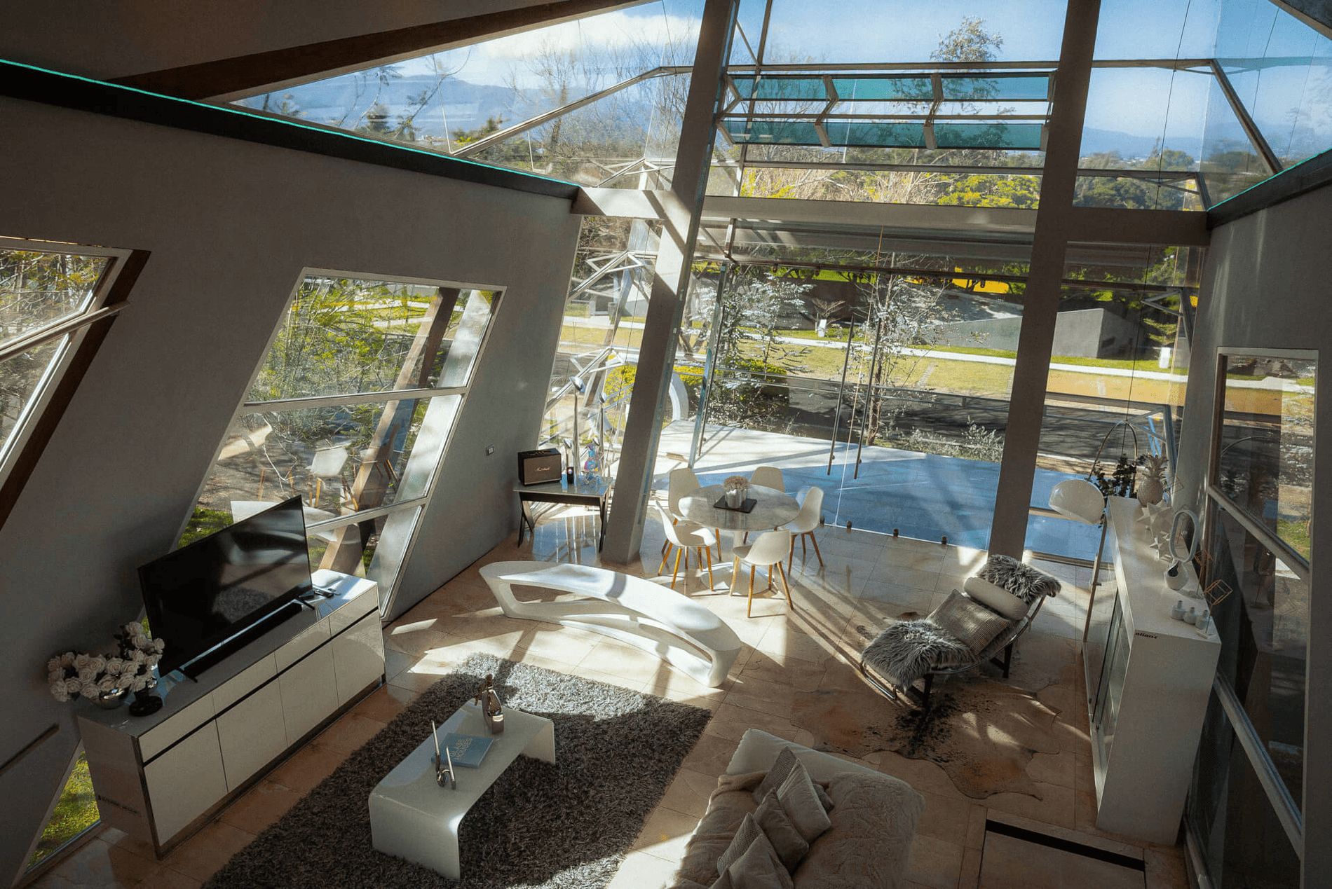 A modern living room with a glass ceiling, a flat-screen TV, a dining table, and a sofa.
