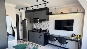 A modern kitchen with dark cabinets, a built-in microwave, and a large TV. There is a dining area with a small table and chairs.