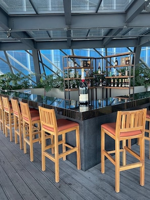 Un espace bar dotĂ© dâun comptoir Ă plateaux en verre, de chaises en bois et dâĂ©tagĂšres remplies de bouteilles.