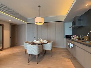 Un espace repas moderne avec une table ronde, deux chaises, un luminaire suspendu et une cuisine équipée d’un évier et d’un plan de travail.