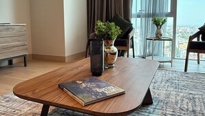 Et moderne hotelværelse med et træbord, en potteplante, en vase og udsigt over byen gennem store vinduer.