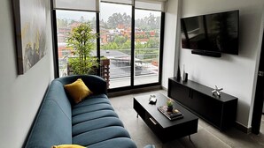 A modern living room with a blue sofa, a coffee table, and a flat-screen TV mounted on the wall. - Modern Apartment with A/C - Steps from Ciudad Cayala & US Embassy (Ciudad de Guatemala)