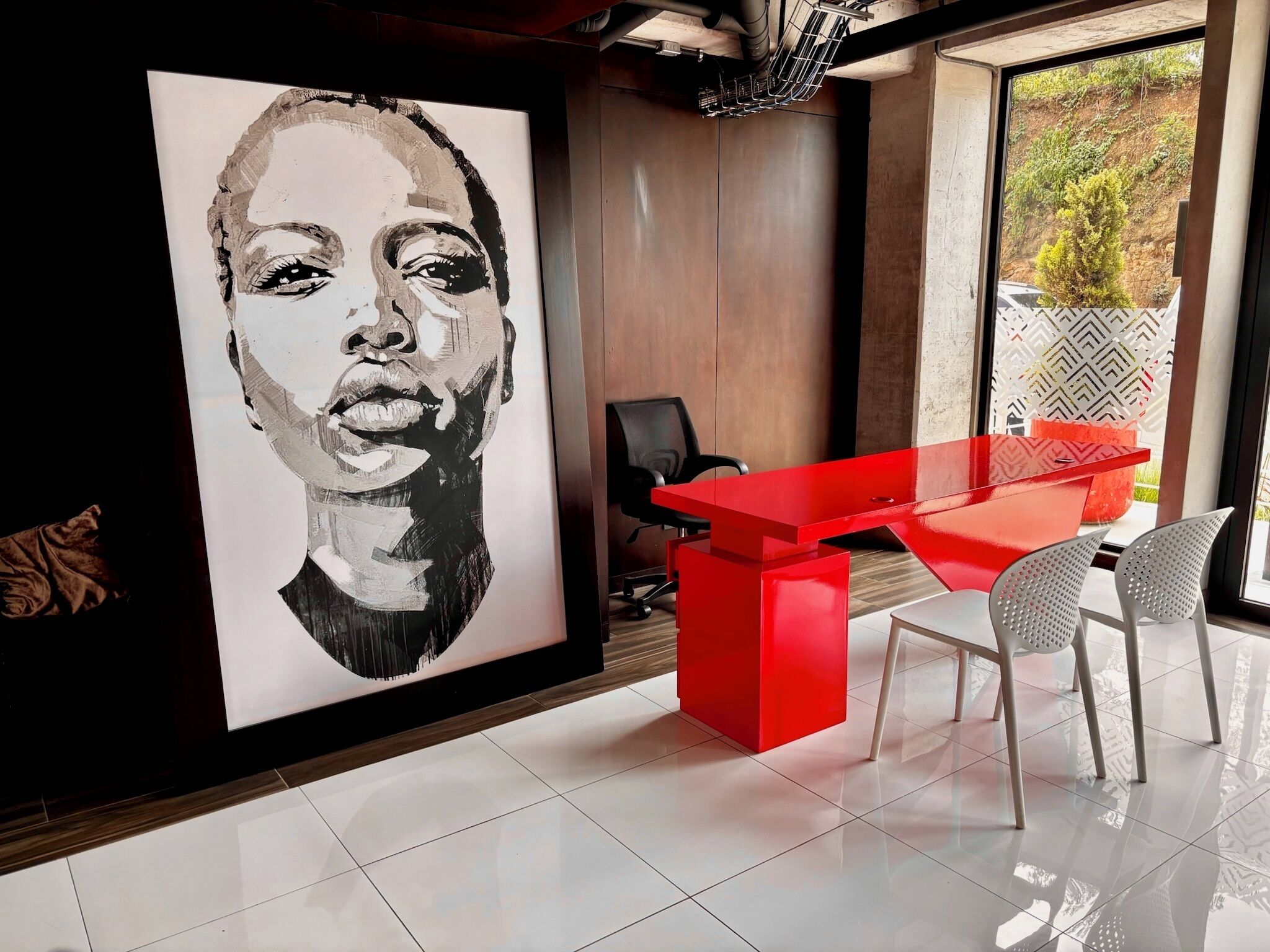 A modern office space with a large black and white portrait on the wall, a red desk, and two white chairs.