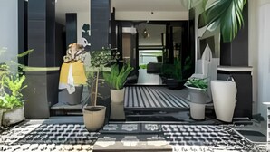Una entrada de edificio moderna con un camino adoquinado, plantas en macetas y una zona de estar.