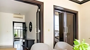 Una sala de estar moderna con un amplio ventanal corredera que da a un balcón. Hay dos sillones blancos con cojines rojos, una mesa de centro y un televisor montado en la pared.