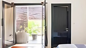 Un dormitorio moderno con una cama grande, un ventanal corredero que da a un balcón y una puerta oscura.