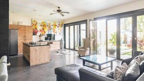 Un espacio de estar moderno con cocina, comedor y un amplio ventanal corredera que da a un jardín.