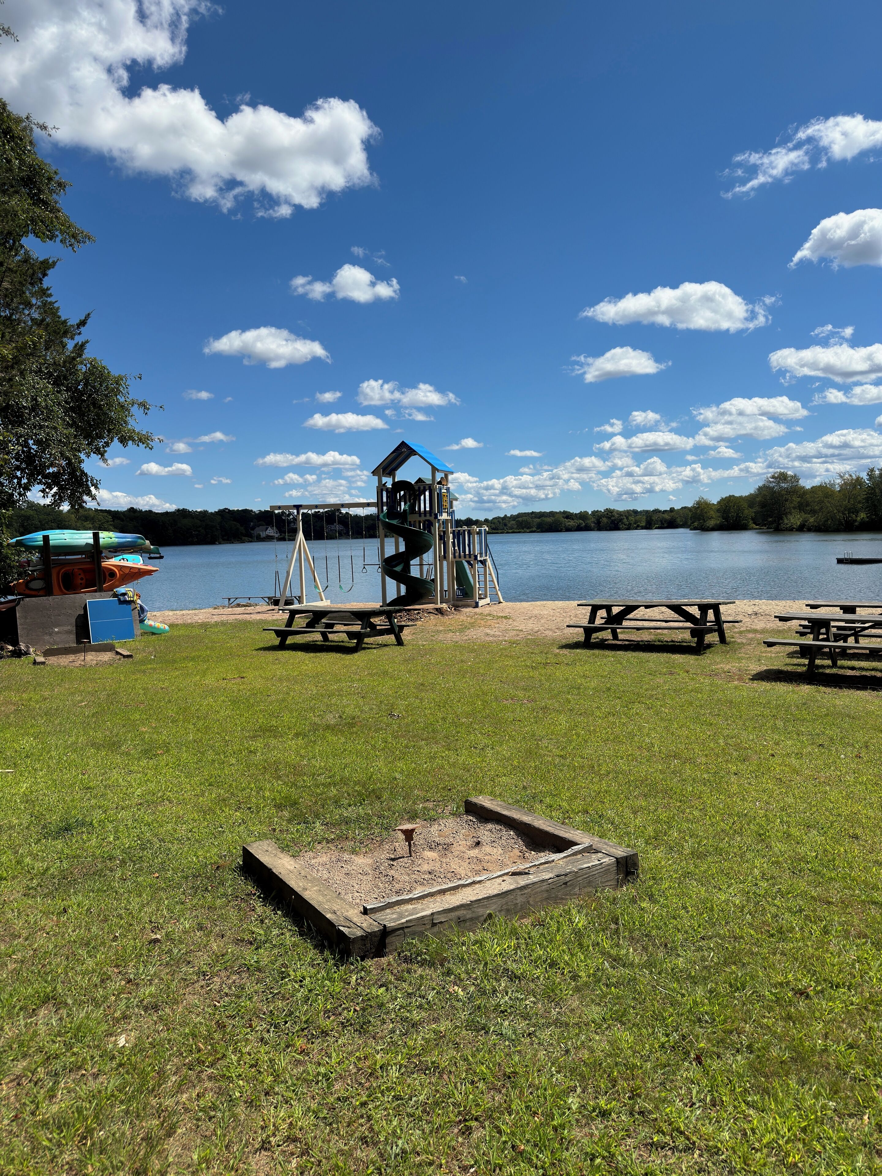 A lakeside park with picnic tables, a playground, and kayaks.