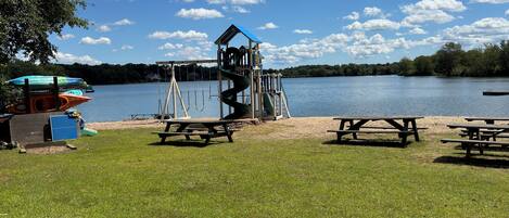 A lakeside park with picnic tables, a playground, and kayaks.