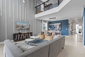 Una sala de estar moderna con un sofá seccional gris, una mesa de centro redonda y un comedor con una pared de acento azul.