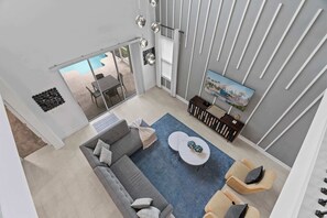 Una sala de estar moderna con un sofá gris, una mesa de centro y un televisor en la pared. Hay un balcón con vista a la piscina.
