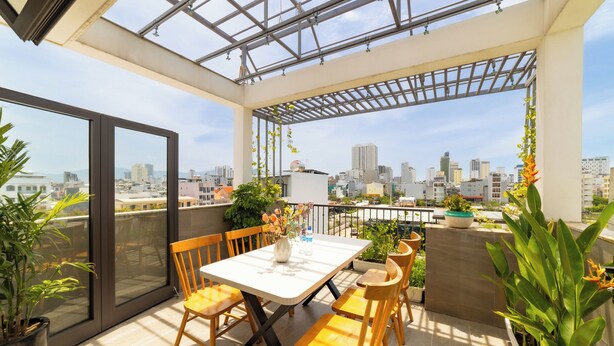 A rooftop terrace with a table and chairs, potted plants, and a city view.