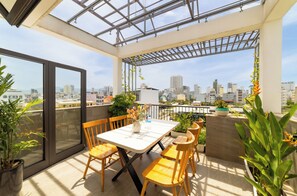 Une terrasse sur le toit, avec une table et des chaises, des plantes en pot et une vue sur la ville.