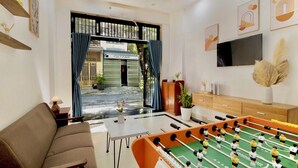 A modern living room with a sofa, a foosball table, a TV, and a view of the street outside.