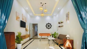 A modern living room with a sofa, a coffee table, a TV mounted on the wall, and a ship's wheel decoration.