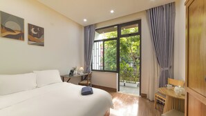 A hotel room with a large bed, a desk with a chair, a small table with a chair, and a view of the outdoors.