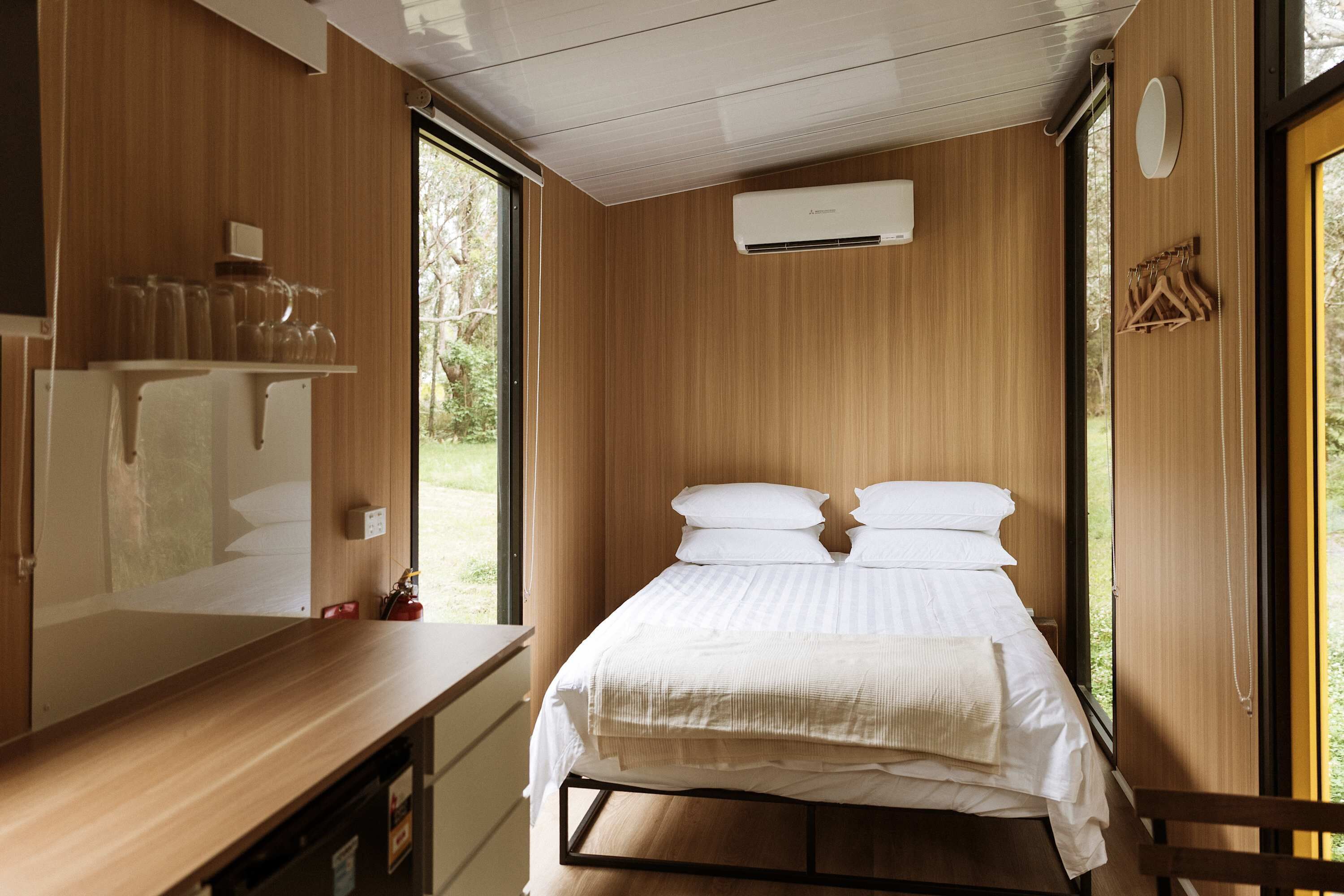 Une chambre avec un mur en bois, un lit avec une literie blanche, une fenêtre et un appareil de climatisation.