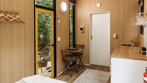 Habitación compacta con interior de madera, una kitchenette pequeña, una mesa plegable y una puerta que da a un espacio al aire libre.