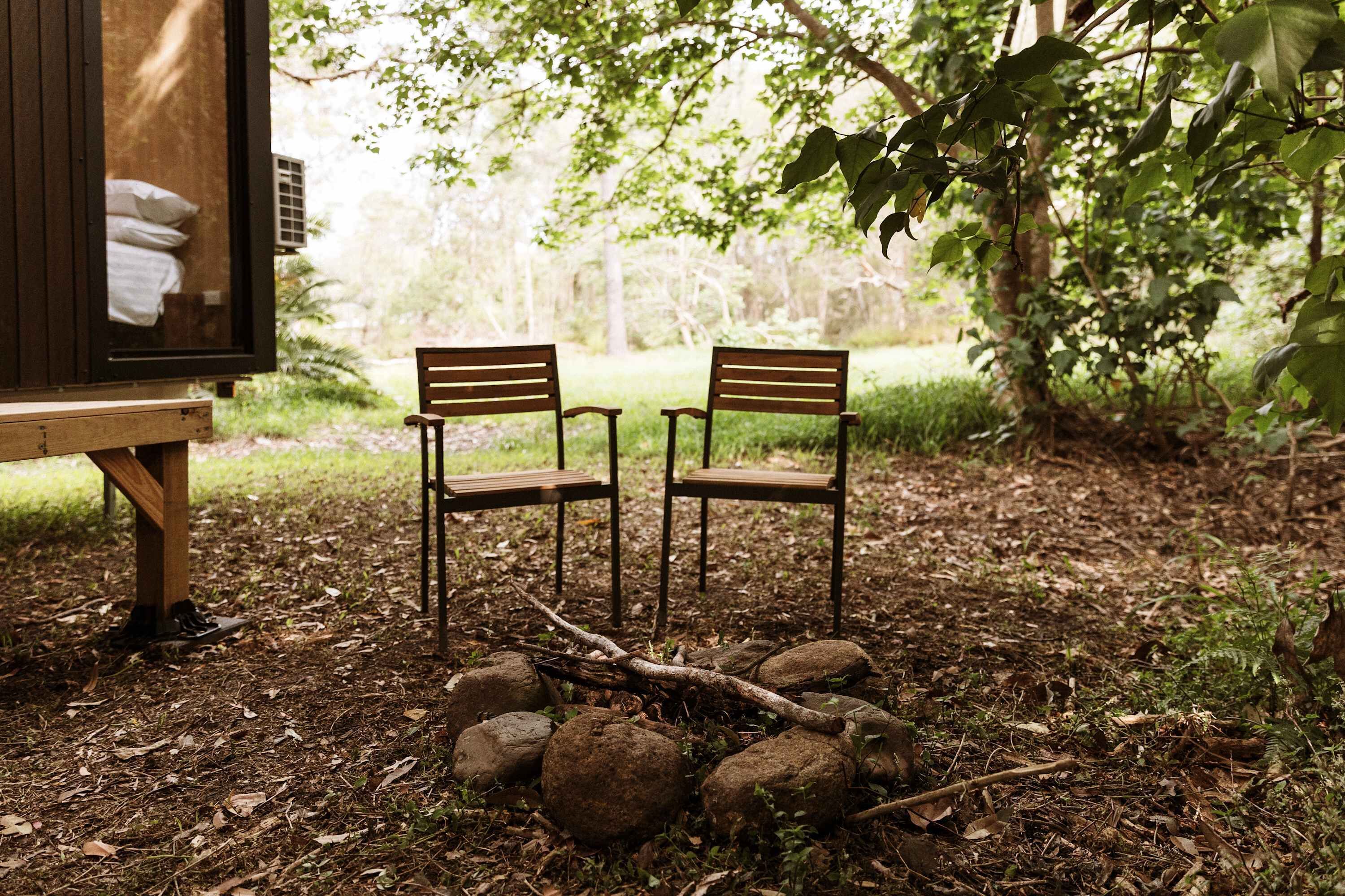 Two wooden chairs under a wooden structure with a view of a forested area.
