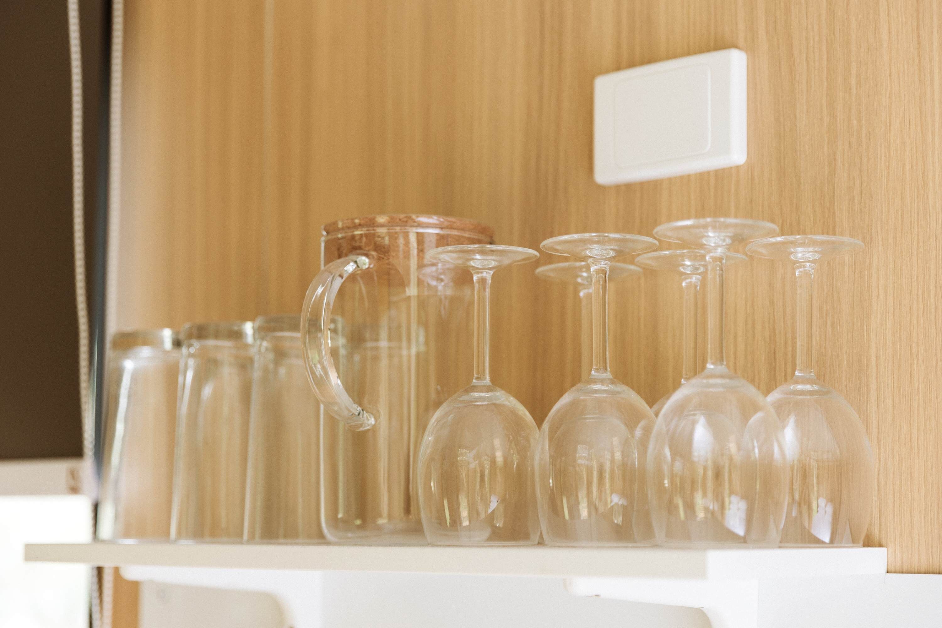 A shelf with various glassware, including a pitcher and wine glasses, against a wooden background.