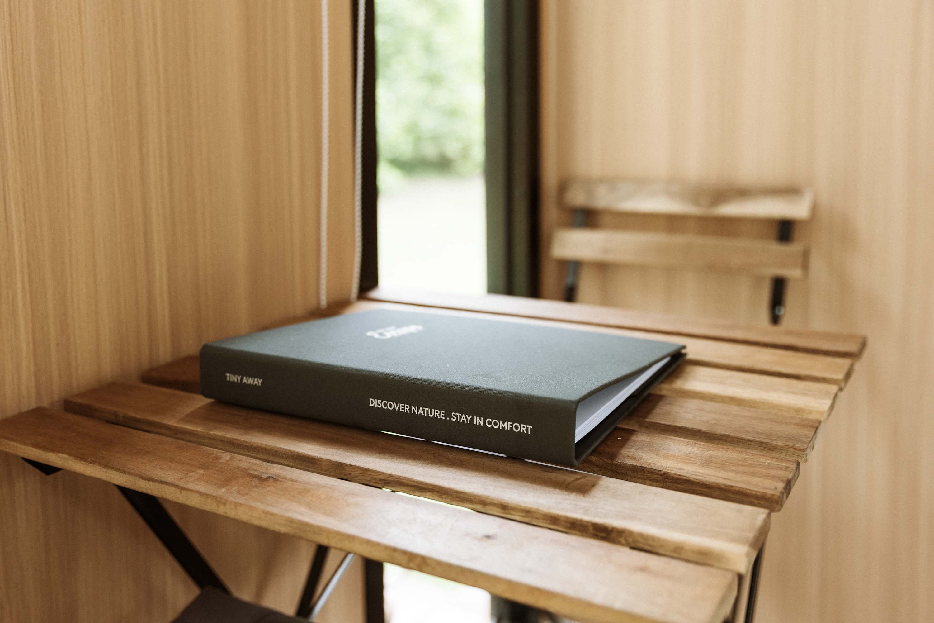 Un libro con el título "Discover Nature - Stay in Comfort" sobre una mesa de madera cerca de una ventana.