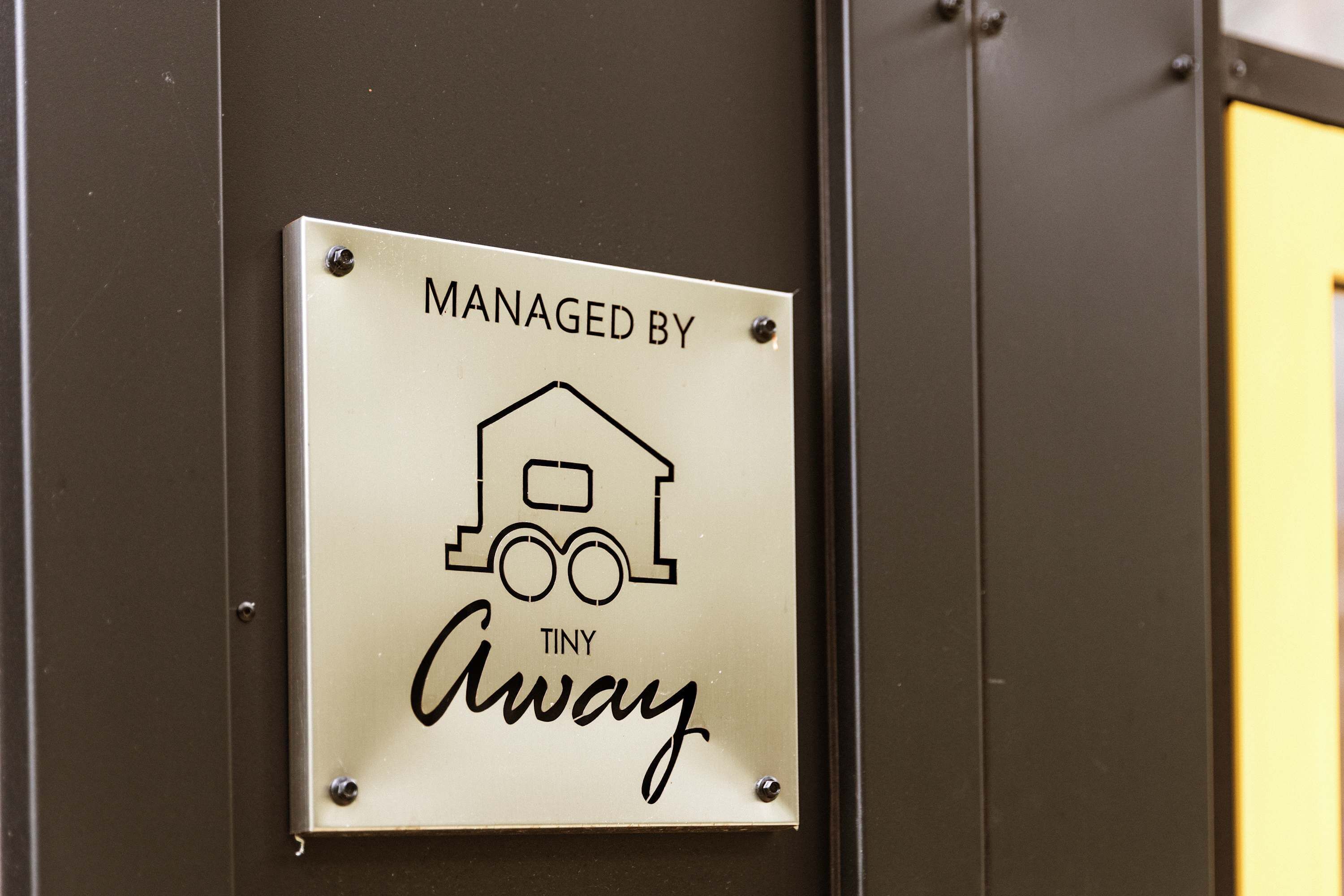 Une pancarte avec le texte « GÉRÉ PAR TINY Away » et un simple pictogramme représentant une maison et un train.
