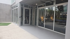Un bâtiment moderne doté de grandes portes vitrées, d’une façade en béton et d’un espace extérieur aménagé avec des tables et des chaises.