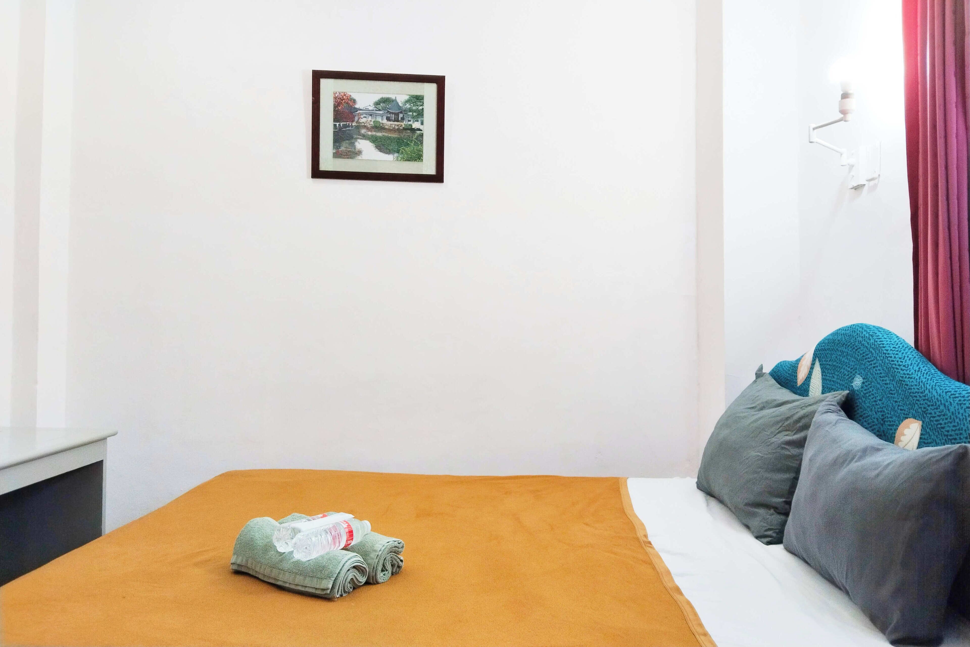 A neatly made bed with a brown bedspread, a rolled-up towel, and a framed picture on the wall.
