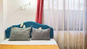 Un lit avec un matelas blanc et une tête de lit turquoise, deux oreillers et un rideau rouge partiellement tiré sur le côté.