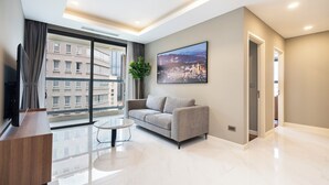 A modern living room with a grey sofa, a glass coffee table, and a large window offering a city view. - The Collection Madison Tower (Ho Chi Minh City)