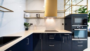 A modern kitchen with dark blue cabinets, a stainless steel sink, a built-in oven, and a range hood. - The Collection Madison Tower (Ho Chi Minh City)