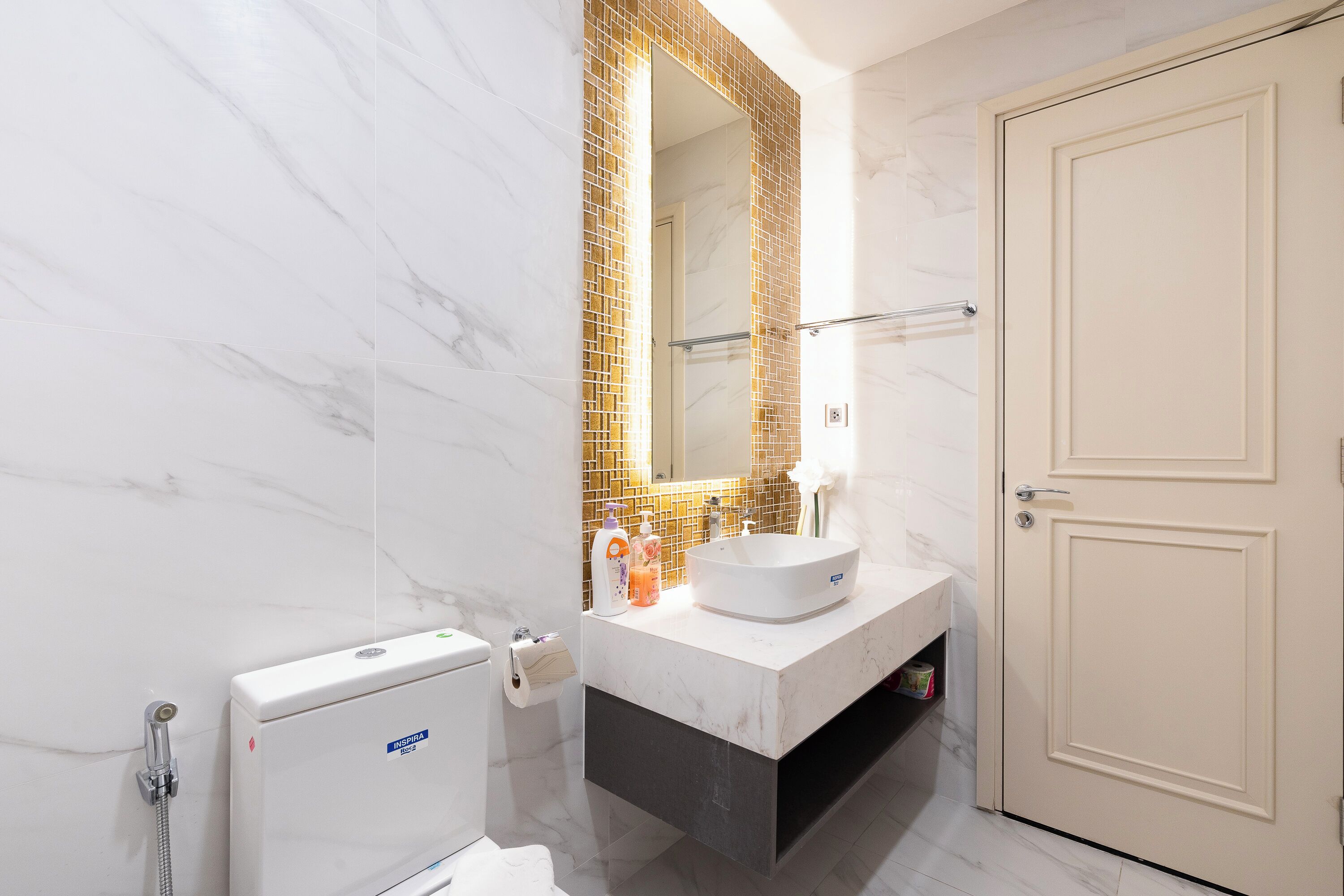 Un baño moderno con lavamanos de mármol blanco, cabina de ducha de vidrio y puerta color beige.