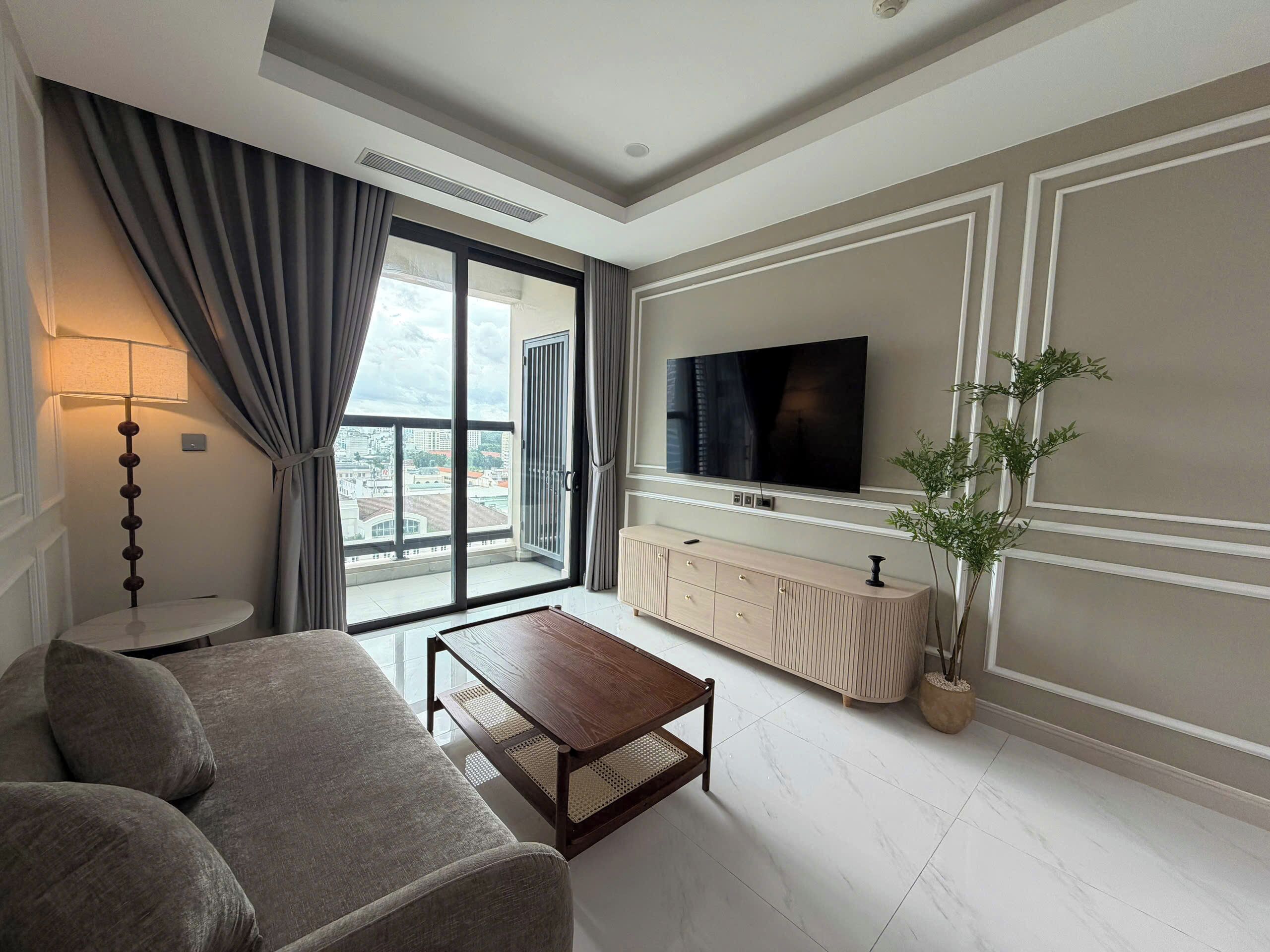 A modern living room with a sofa, a coffee table, a TV, and a large window with curtains.