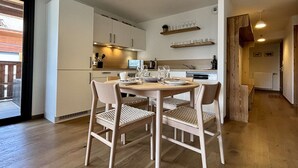 A modern kitchen with white cabinets, a dining table with chairs, and a hanging light fixture.