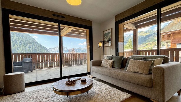 A spacious living room with a large sofa, a round coffee table, and a view of mountains through large windows.