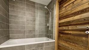 A modern bathroom with a bathtub, shower, and wooden door.