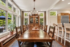 A spacious dining area with a long wooden table, multiple chairs, and a chandelier.