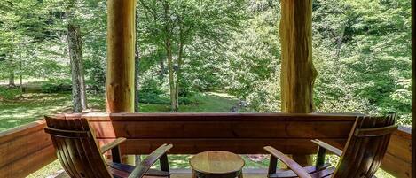 A wooden deck with a bench and two rocking chairs, overlooking a forested area.