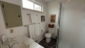 Un baño con lavamanos blanco, un espejo, una ventana, inodoro y ducha.