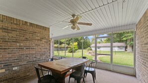 Un patio techado con pared de ladrillo, una mesa de madera, cuatro sillas y un ventilador de techo.