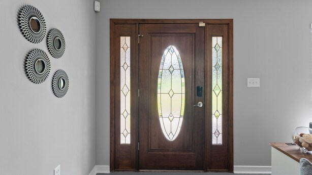 Una puerta de madera con un panel de vidrio y detalles metálicos decorativos en la pared.
