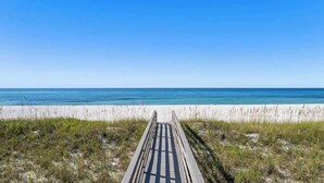 A wooden boardwalk leading to a beach with clear blue water and white sand. - The Drift Away (Navarre Beach)